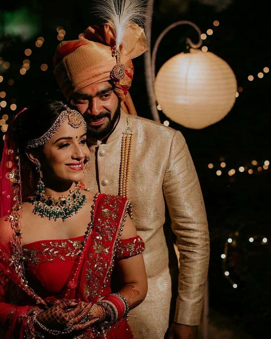 AI generated Indian groom dressed in white Sherwani and red hat with  stunning bride in red lehenga stand and hold each hands walking outside  34797758 Stock Photo at Vecteezy